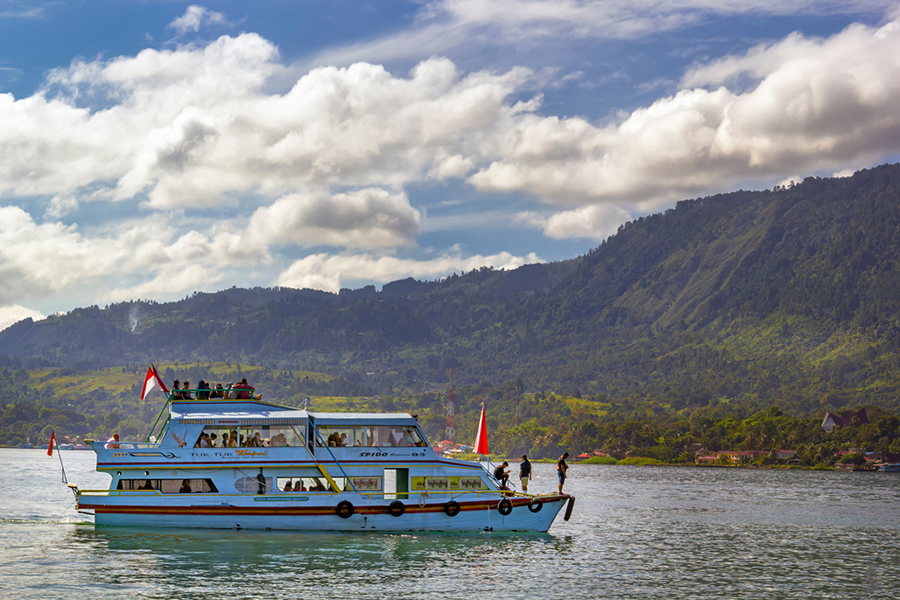 Pleasure boat goes on the water against the backdrop of mountains and sky with clouds on a sunny day
